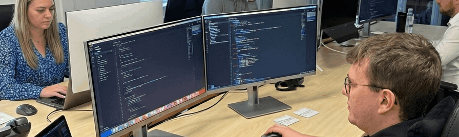 NYBE professionele I.T. in Hasselt custom software development kantoor medewerkers met focus op man in voorgrond werkend op computer die code toont